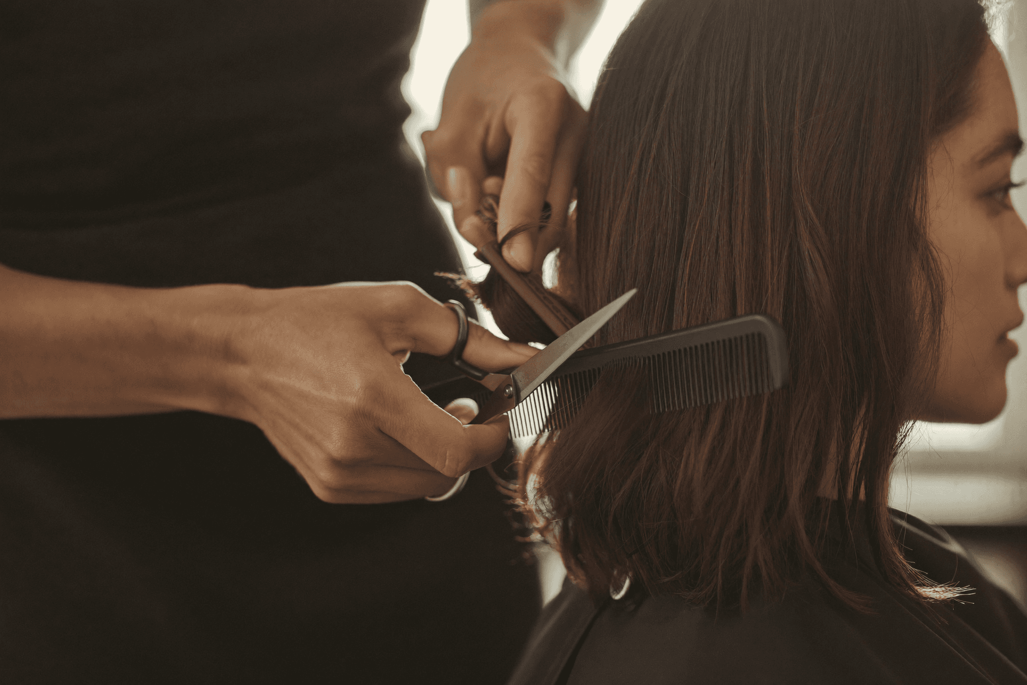 Hände einer Friseurin, die mit Schere und Kamm mittellanges Haar schneiden